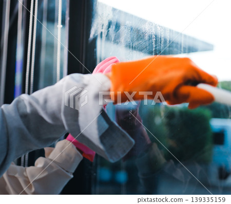 Person cleaning the room, cleaning staff is using cloth and spraying disinfectant to wipe the tables in the company office room. Cleaning staff. Maintaining cleanliness in the organization. 139335159