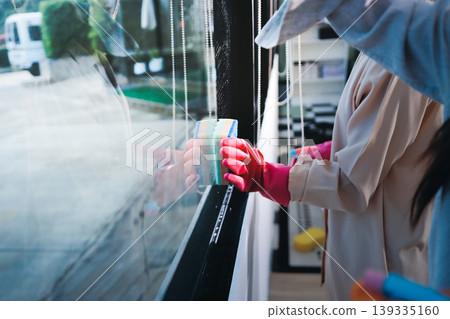 Person cleaning the room, cleaning staff is using cloth and spraying disinfectant to wipe the tables in the company office room. Cleaning staff. Maintaining cleanliness in the organization. Person cleaning the room, cleaning staff is using cloth and spraying disinfectant to wipe the tables in the company office room. Cleaning staff. Maintaining cleanliness in the organization. 139335160