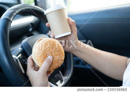 Asian woman driver hold and eat hamburger in car, dangerous and risk an accident. 139336960