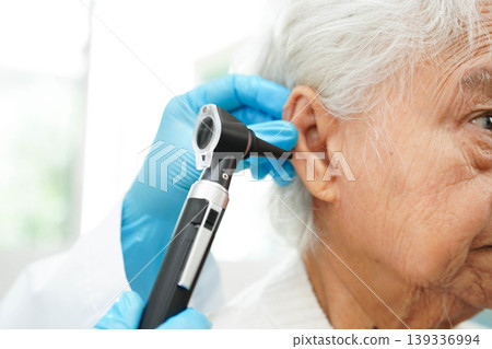 Otolaryngologist or ENT physician doctor examining senior patient ear with otoscope, hearing loss problem. Otolaryngologist or ENT physician doctor examining senior patient ear with otoscope, hearing loss problem. 139336994