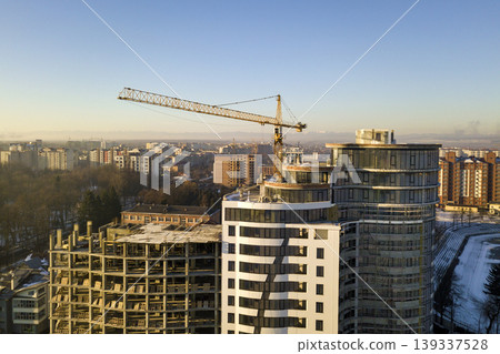 Apartment or office tall building under construction, top view. Tower crane on bright blue sky copy space background, city landscape stretching to horizon. Drone aerial photography. Apartment or office tall building under construction, top view. Tower crane on bright blue sky copy space background, city landscape stretching to horizon. Drone aerial photography. 139337528