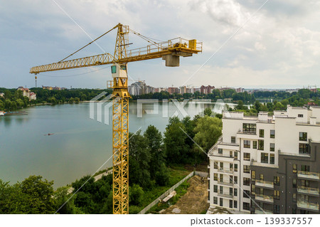 Aerial view of tower lifting crane and concrete frame of tall apartment residential building under construction in a city. Urban development and real estate growth concept. Aerial view of tower lifting crane and concrete frame of tall apartment residential building under construction in a city. Urban development and real estate growth concept. 139337557
