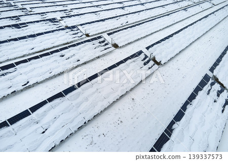 Aerial view of snow covered sustainable electric power plant with rows of solar photovoltaic panels for producing clean electrical energy. Low effectivity of renewable electricity in northern winter Aerial view of snow covered sustainable electric power plant with rows of solar photovoltaic panels for producing clean electrical energy. Low effectivity of renewable electricity in northern winter 139337573
