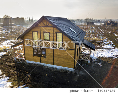 Aerial view of new wooden ecological traditional house cottage of natural lumber materials with steep shingle roof under construction on winter rural landscape background. Aerial view of new wooden ecological traditional house cottage of natural lumber materials with steep shingle roof under construction on winter rural landscape background. 139337585