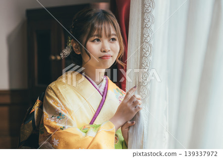 A 20-year-old woman in a furisode kimono gazes out the window of a retro, antique Western-style mansion/studio. 139337972