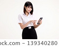 Happy young Asian woman in student uniform using smartphone and touching the screen. Smiling female university student holding mobile phone and browsing social media, isolated on white background. 139340280