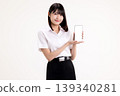Smiling young Asian woman in student uniform presenting a smartphone with white blank screen. Happy female university student holding mobile phone mockup for app or website display. 139340281