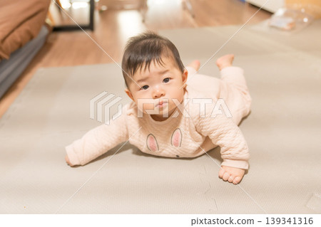 A Japanese baby boy in a rabbit-patterned romper lies face down and looks at the camera. A Japanese baby boy in a rabbit-patterned romper lies face down and looks at the camera. 139341316