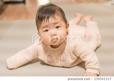 A Japanese baby boy in a rabbit-patterned romper lies face down and looks at the camera. A Japanese baby boy in a rabbit-patterned romper lies face down and looks at the camera. 139341317