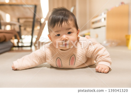 A Japanese baby boy in a rabbit-patterned romper lies face down and looks at the camera. 139341320