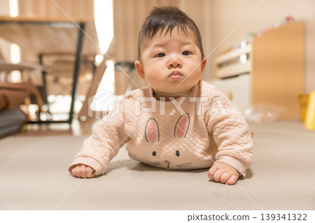 A Japanese baby boy in a rabbit-patterned romper lies face down and looks at the camera. A Japanese baby boy in a rabbit-patterned romper lies face down and looks at the camera. 139341322