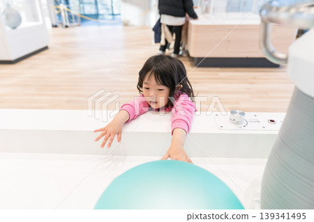 A young Japanese girl playing with exhibits at a science museum. A young Japanese girl playing with exhibits at a science museum. 139341495
