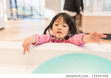 A young Japanese girl playing with exhibits at a science museum. A young Japanese girl playing with exhibits at a science museum. 139341496