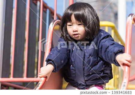 A Japanese toddler girl slides down a slide in a park. A Japanese toddler girl slides down a slide in a park. 139341683