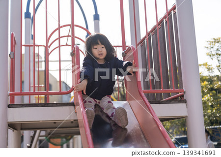 A Japanese toddler girl slides down a slide in a park. A Japanese toddler girl slides down a slide in a park. 139341691