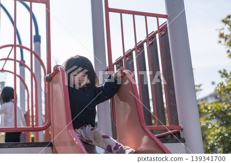 A Japanese toddler girl slides down a slide in a park. 139341700