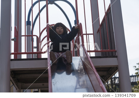 A Japanese toddler girl slides down a slide in a park. A Japanese toddler girl slides down a slide in a park. 139341709