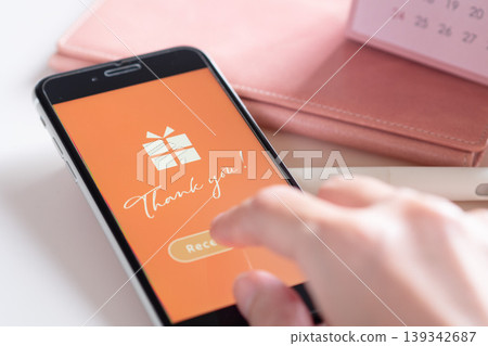 A woman's hand taps the screen to receive a social gift (e-gift) that arrived on her smartphone. (Image) A woman's hand taps the screen to receive a social gift (e-gift) that arrived on her smartphone. (Image) 139342687