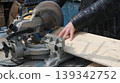 Processing a wide board on a miter saw, close-up view from the top side angle, a carpenter saws off a part of the board on the end machine 139342752