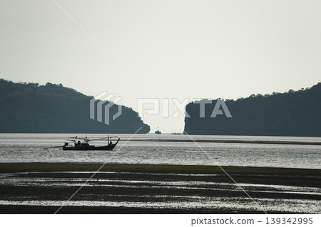 Silhouette of long-tail boat floating in the calm sea in front of the space between two islands 139342995