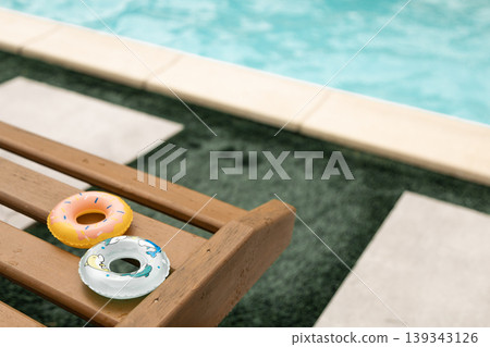 Colorful mini pool floats on a wet wooden deck chair by blurred turquoise swimming pool water 139343126