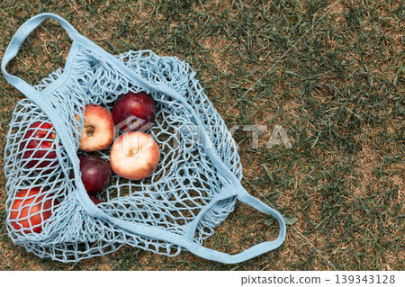 Fresh summer fruits in blue reusable net bag on green grass Fresh summer fruits in blue reusable net bag on green grass 139343128