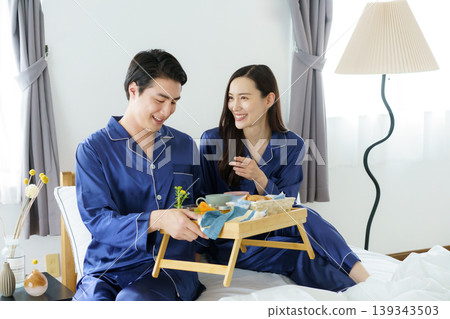A young Japanese celebrity couple tries to eat breakfast side-by-side in bed in the morning. A young Japanese celebrity couple tries to eat breakfast side-by-side in bed in the morning. 139343503
