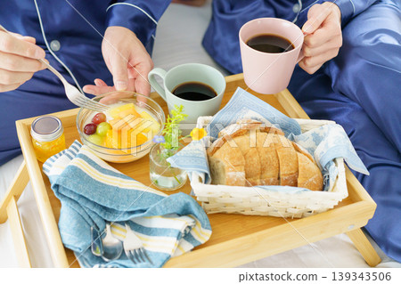 Close-up of a man and woman eating breakfast placed on a bedside table. Close-up of a man and woman eating breakfast placed on a bedside table. 139343506