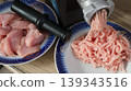 On the kitchen counter is a black electric meat grinder and two dishes containing pink chicken fillets and ready-made minced meat, ground in a household appliance for making homemade minced meat 139343516