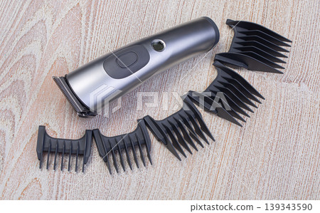 Electric hair clipper with various guard combs on wooden background 139343590
