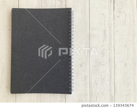 A ring-bound notebook with a black cover, set against a wood-grain background, is featured in a lifestyle and business-themed setting. 139343674