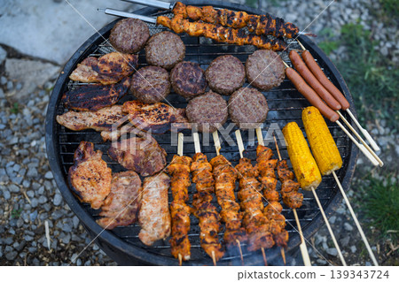 Variety of grilled meat, burgers, sausages and corn on barbecue grill outdoors, summer BBQ food cooking concept Variety of grilled meat, burgers, sausages and corn on barbecue grill outdoors, summer BBQ food cooking concept 139343724