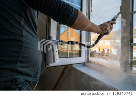 Cleaning the window. A man with steam device removes dirt from the plastic window frame. Cleaning the window. A man with steam device removes dirt from the plastic window frame. 139343741