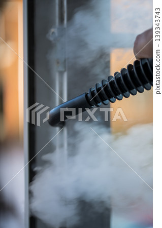 Cleaning the window. A man with steam device removes dirt from the plastic window frame. Cleaning the window. A man with steam device removes dirt from the plastic window frame. 139343743