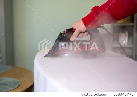 Man's hand ironing clothes on an ironing board at home, copy space Man's hand ironing clothes on an ironing board at home, copy space 139343772