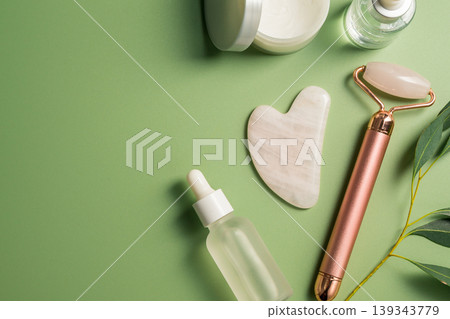Rose quartz gua sha tool and face massage roller on green background, beauty abstract photo. Top view 139343779
