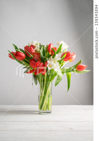 Spring floral background. Red tulips and Fresia white flower bouquet in glass vase. Copy space 139343894