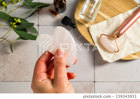 Rose quartz gua sha tool in female hand, face massage tool, beauty abstract photo Rose quartz gua sha tool in female hand, face massage tool, beauty abstract photo 139343931