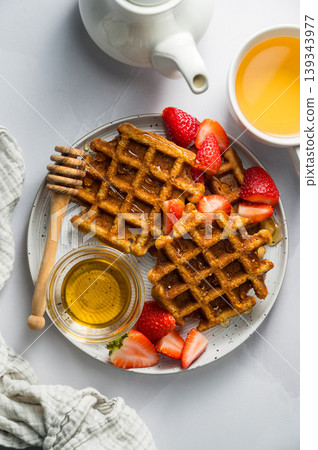 Belgian waffles with strawberries and honey, cup of tea and fresh fruits. Homemade breakfast food, top view Belgian waffles with strawberries and honey, cup of tea and fresh fruits. Homemade breakfast food, top view 139343977
