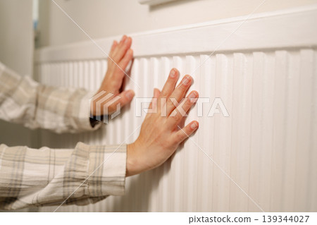 Woman warming up hands over heater. Increasing bills expenses. Cold season. Rising utility costs Woman warming up hands over heater. Increasing bills expenses. Cold season. Rising utility costs 139344027