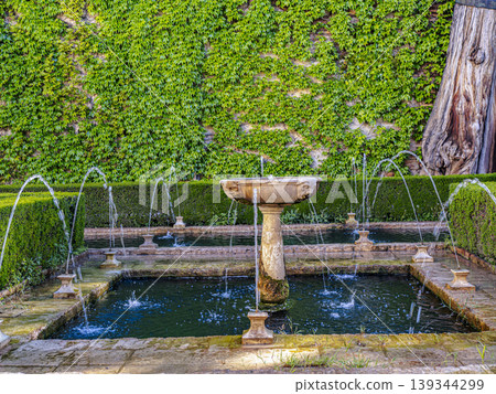 Ornate Stone Fountain in Alhambra Generalife Gardens With Arched Water Jets at Sunset, Granada 139344299