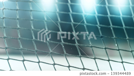 Close-up detail of an ice hockey goal net inside an indoor rink, with shallow depth of field and blurred background, capturing sports atmosphere and texture of the net mesh. Close-up detail of an ice hockey goal net inside an indoor rink, with shallow depth of field and blurred background, capturing sports atmosphere and texture of the net mesh. 139344489