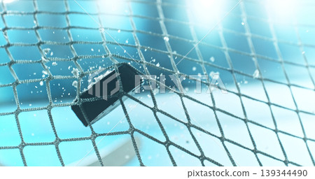Action sports photo of a hockey puck flying into the goal net during a scoring shot, with ice particles in the air and a hockey stick visible in the background, capturing speed and intensity. Action sports photo of a hockey puck flying into the goal net during a scoring shot, with ice particles in the air and a hockey stick visible in the background, capturing speed and intensity. 139344490