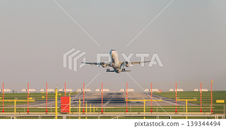 Front view of a commercial passenger airplane taking off from airport runway with visible heat haze and clear sky. Aviation, travel and transportation concept. Front view of a commercial passenger airplane taking off from airport runway with visible heat haze and clear sky. Aviation, travel and transportation concept. 139344494