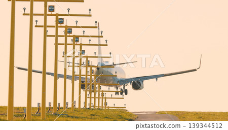 Passenger airplane approaching runway aligned with airport approach lighting system during golden hour. Perspective view of aviation infrastructure. 139344512