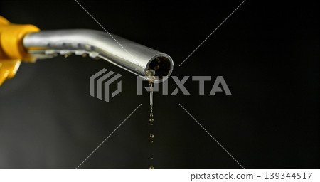 Gasoline drops dripping from fuel nozzle on dark background, minimal fuel flow. Concept of fuel depletion, shortage and energy crisis, macro detail, dramatic lighting. Gasoline drops dripping from fuel nozzle on dark background, minimal fuel flow. Concept of fuel depletion, shortage and energy crisis, macro detail, dramatic lighting. 139344517