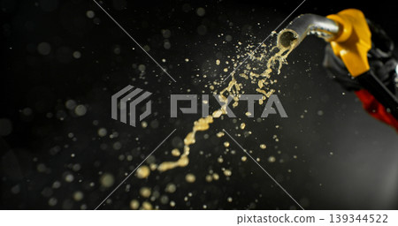 Gasoline jet spraying from fuel nozzle held by hand on dark background. Dynamic liquid motion, refueling concept, energy supply, fuel usage, dramatic lighting, macro detail. 139344522