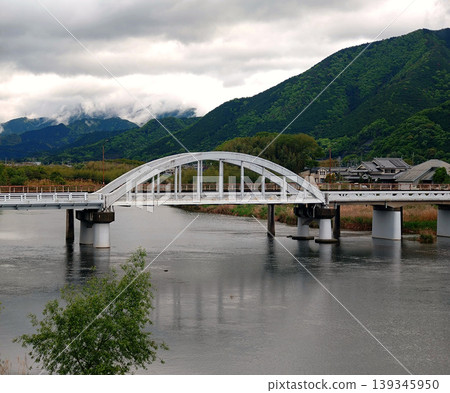 一幅日本風景畫,描繪了雲層籠罩下的山谷中河流蜿蜒而過,一座拱橋橫跨其間。 一幅日本風景畫,描繪了雲層籠罩下的山谷中河流蜿蜒而過,一座拱橋橫跨其間。 139345950