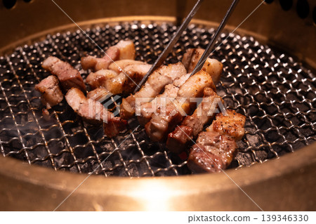Close-up of beef slices and tongs being grilled over charcoal. Close-up of beef slices and tongs being grilled over charcoal. 139346330