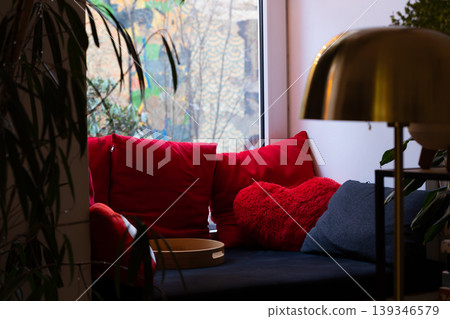 A comfortable seating area by the window, adorned with plush red cushions and a stylish lamp, inviting relaxation and warmth A comfortable seating area by the window, adorned with plush red cushions and a stylish lamp, inviting relaxation and warmth 139346579